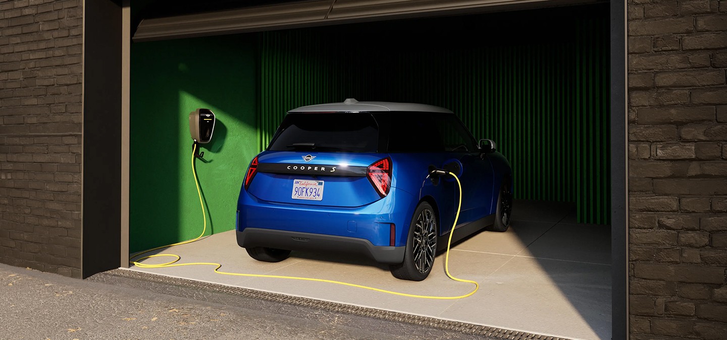 Rear view of Blazing Blue all-electric MINI Cooper in garage with charging cable